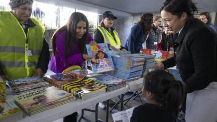 Asm. Ortega at a table giving books to kids at event.